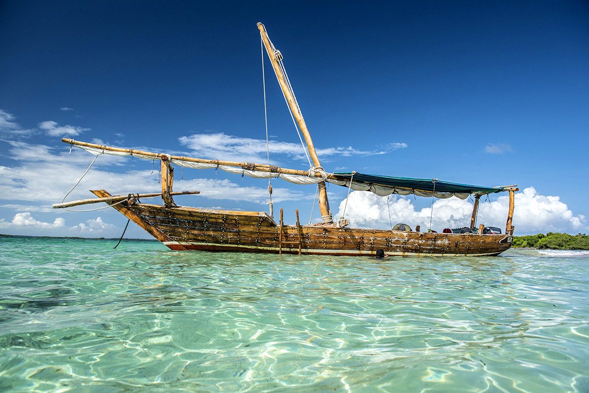 Traditional wooden dhow boat sailing at sunset off Zanzibar